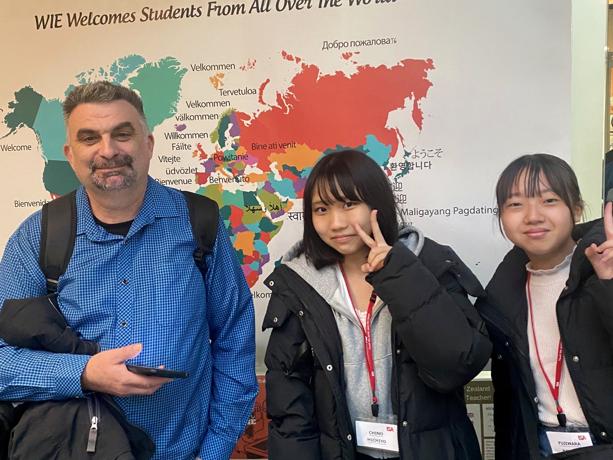 An adult male (staff or homestay host) standing alongside two young female international students with...