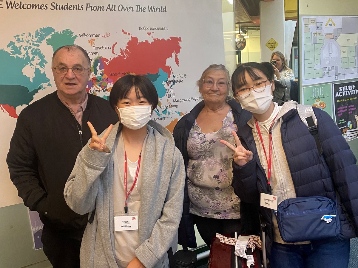 Two international female students wearing WIE/ISA lanyards, name badges, and face masks pose cheerfully...