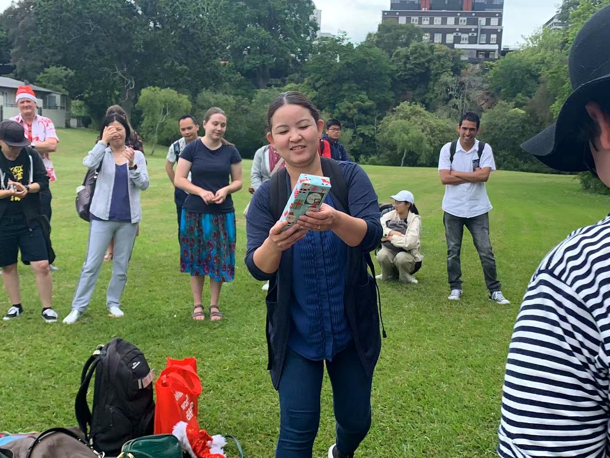 A group of diverse international students and staff participating in an outdoor holiday picnic and gift...