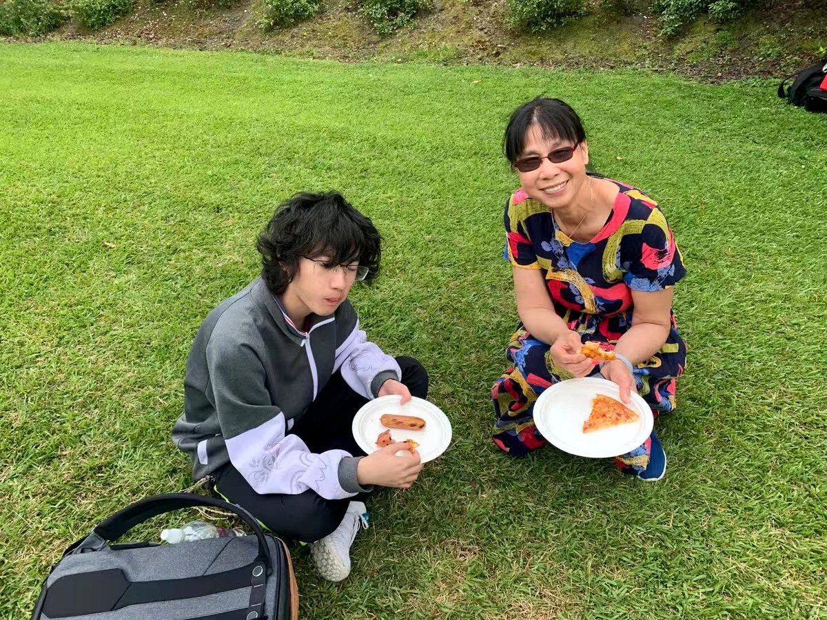 A young student and an older woman sitting on the grass outdoors during a casual social picnic or homestay...