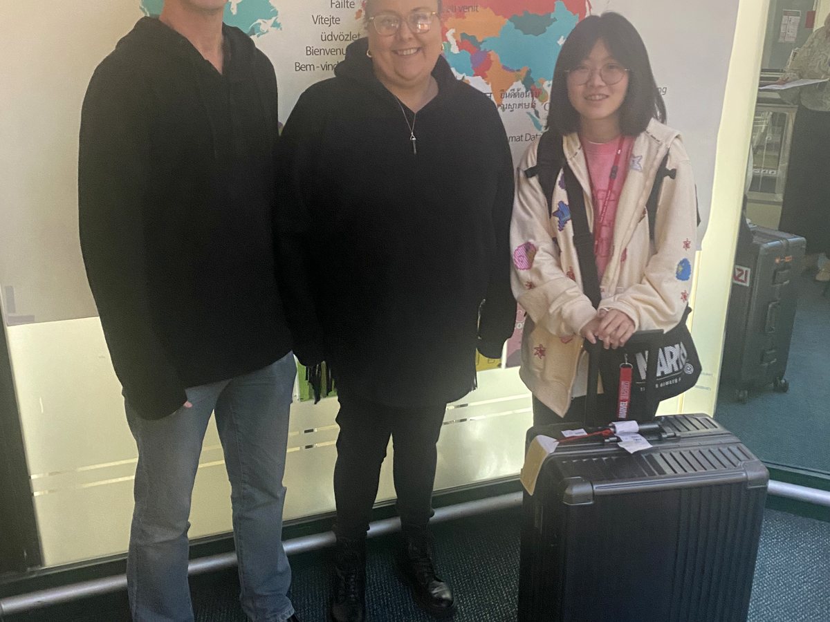 An authentic photo of an international student with a suitcase posing alongside two WIE staff members or...