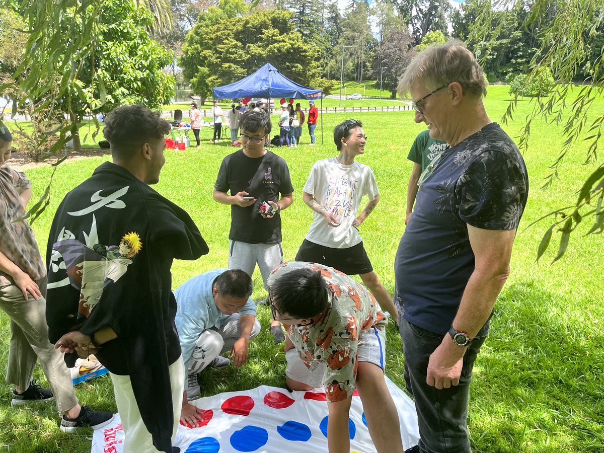 A diverse group of international students and a staff member or teacher engaging in an outdoor Twister...