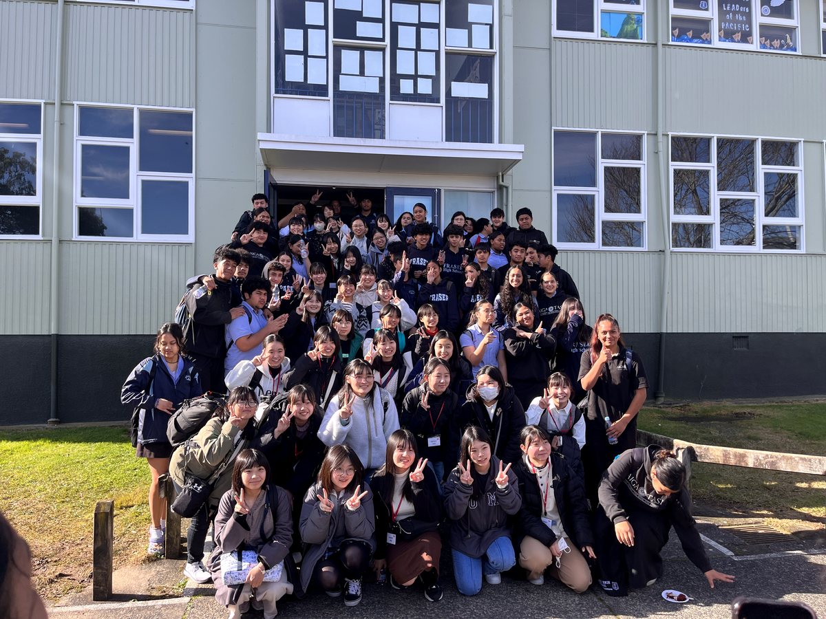 A large group photo of international and local high school students posing together cheerfully outdoors in...