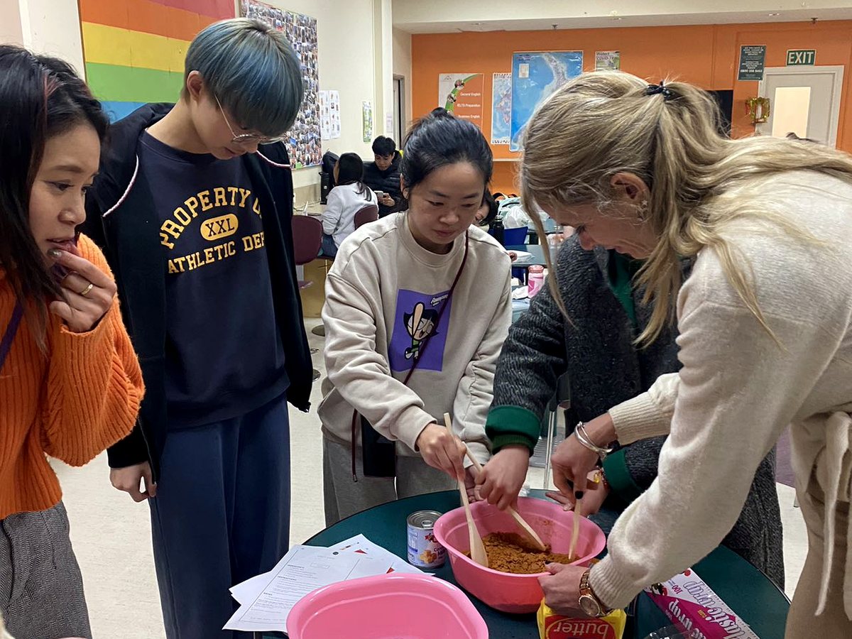 A candid indoor group activity shot showing diverse students and staff mixing ingredients together at a...